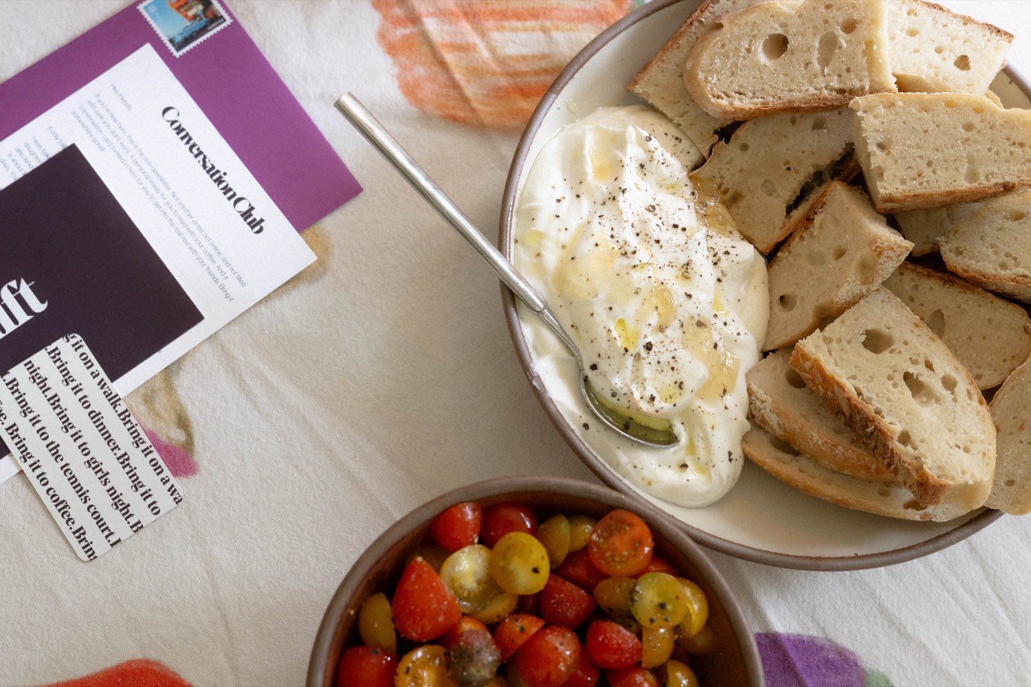 The Conversation Club letter and cards on a table beside fresh bread and burrata